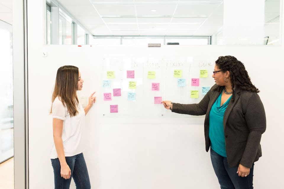 Two colleagues discussing ideas at a glass wall covered in sticky notes