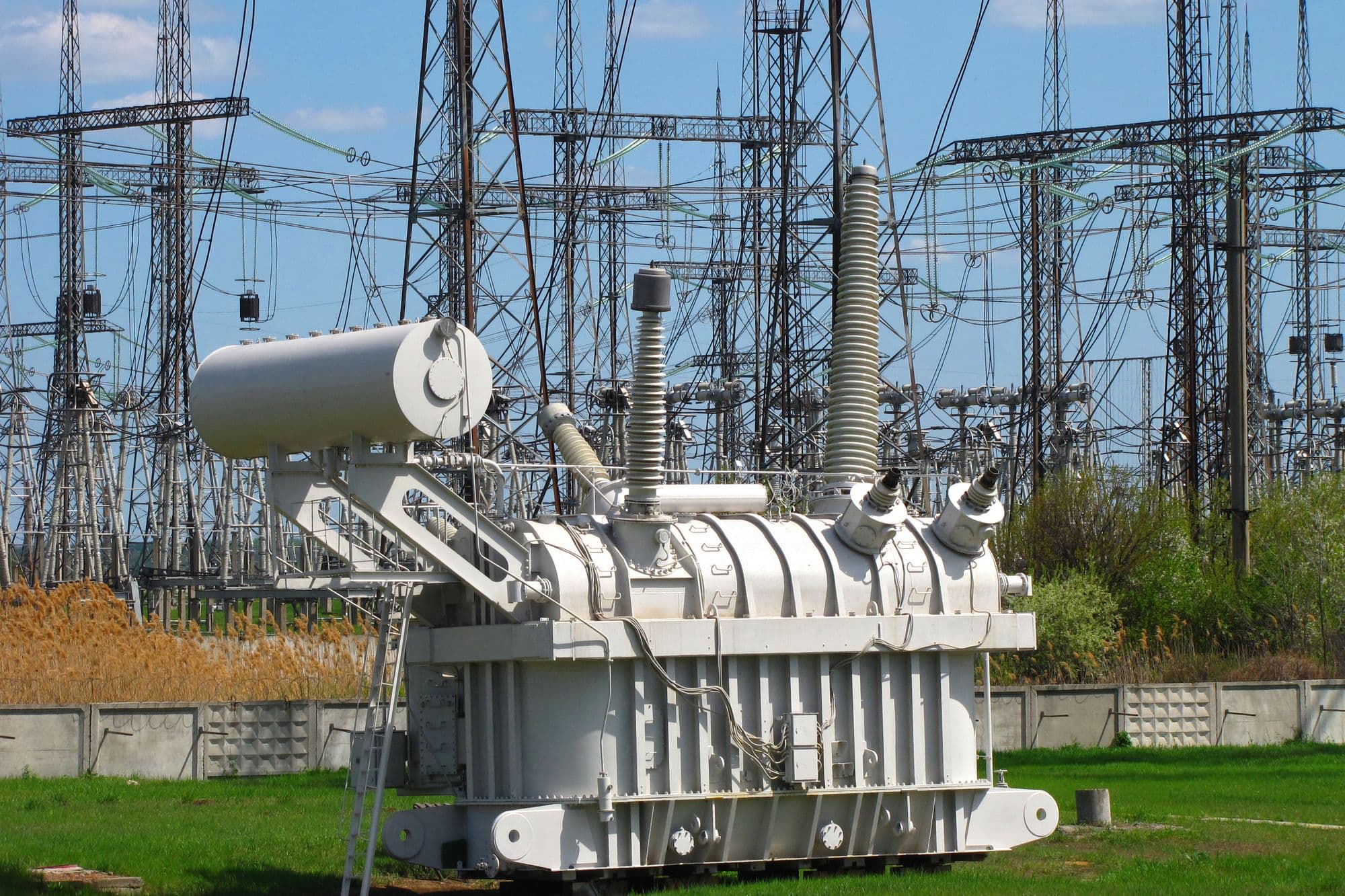 Large high-voltage power transformer in front of the steel lattice gantries of an electrical substation