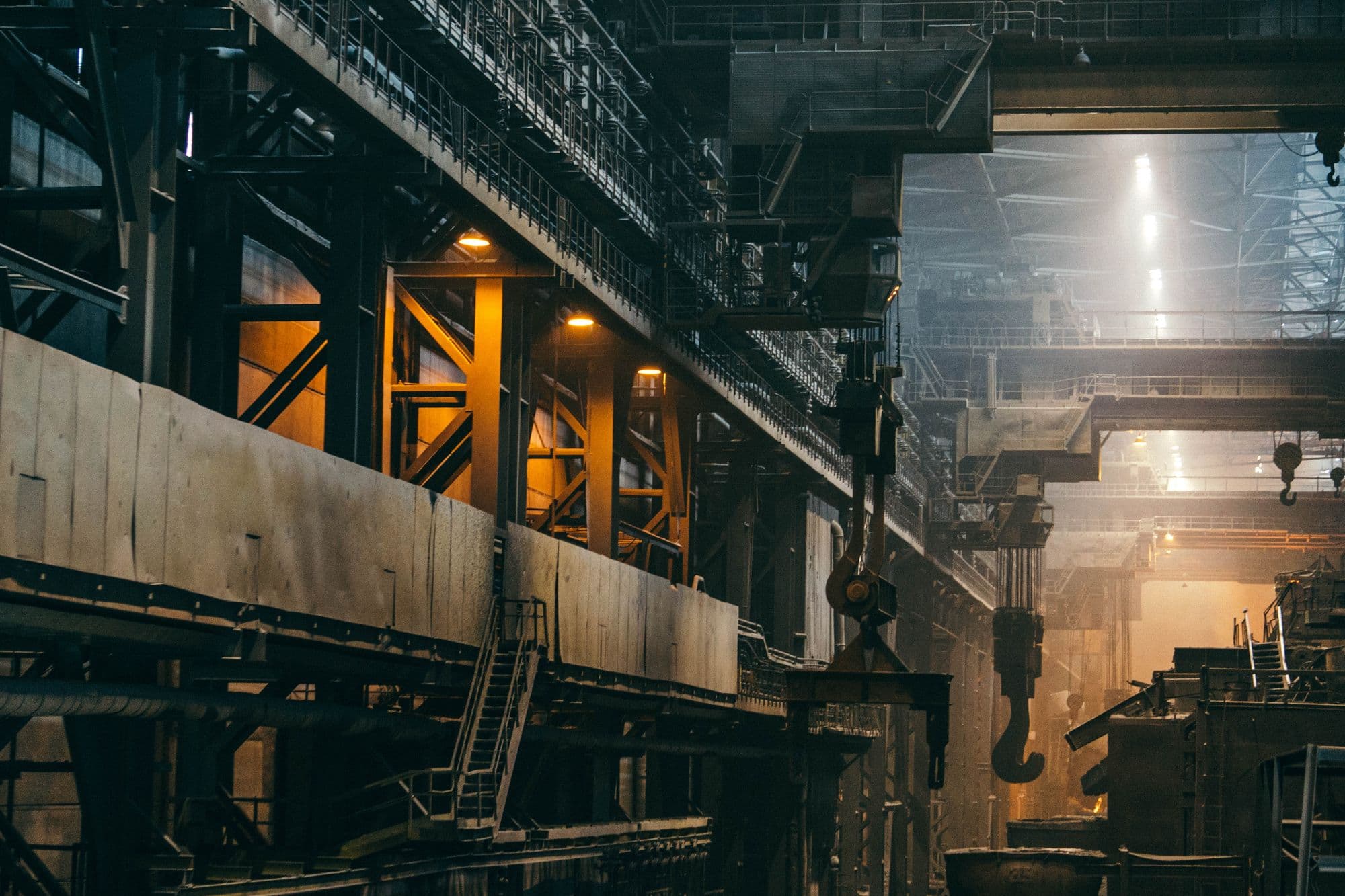 Interior of a heavy industrial plant with overhead cranes, steel gantries and warm hazy light