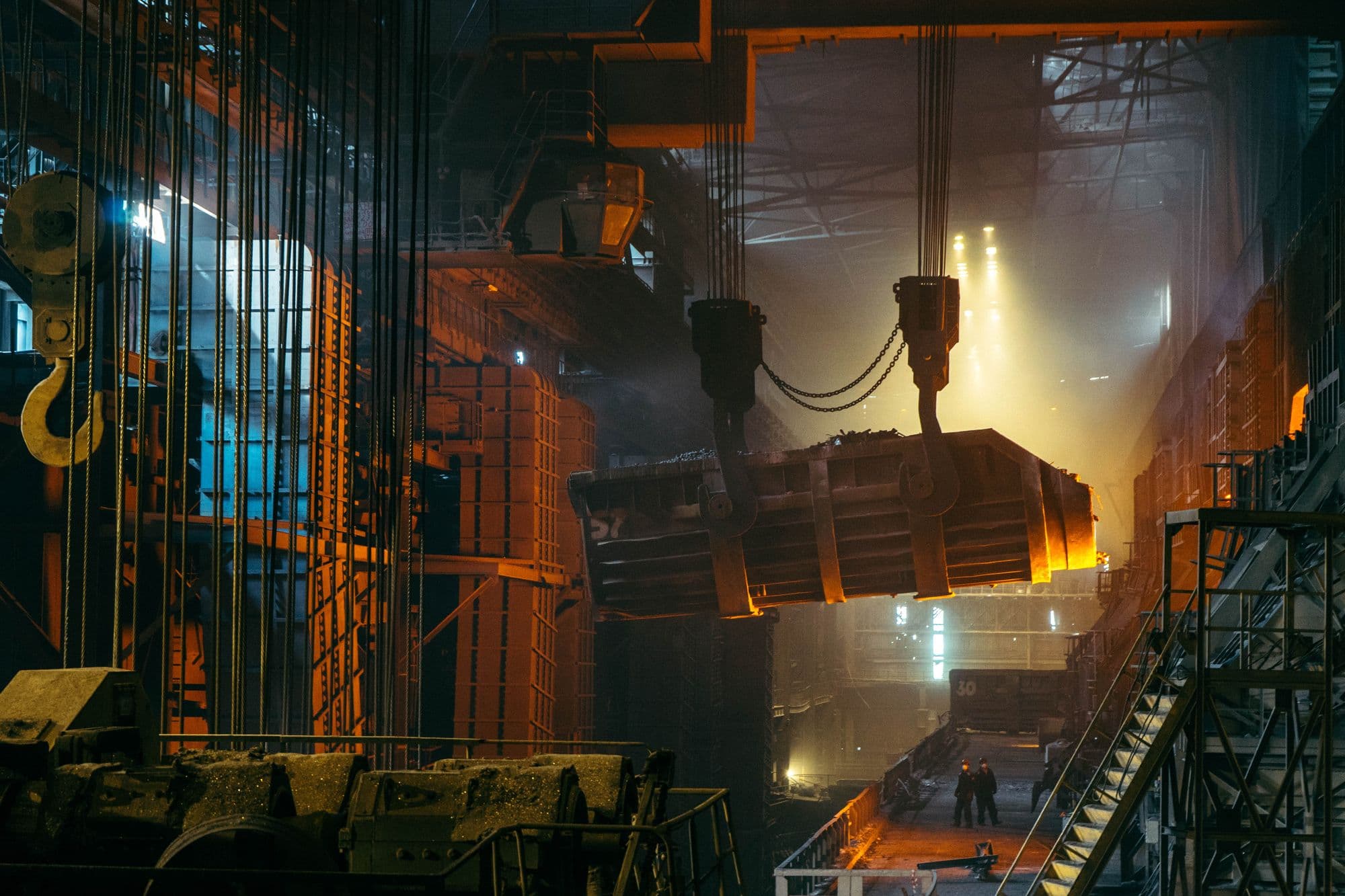 Steelworks interior with a crane carrying a glowing ladle above the furnace floor