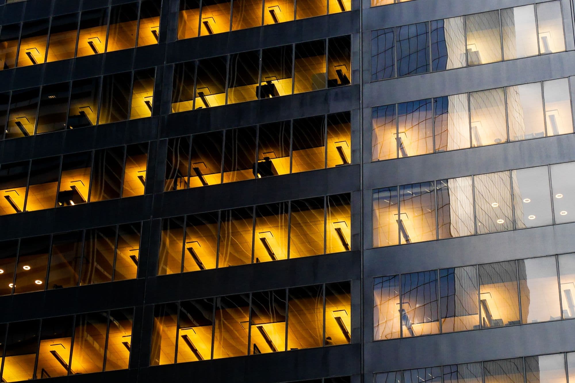 Facade of a modern office building at dusk with warm light glowing from rows of windows
