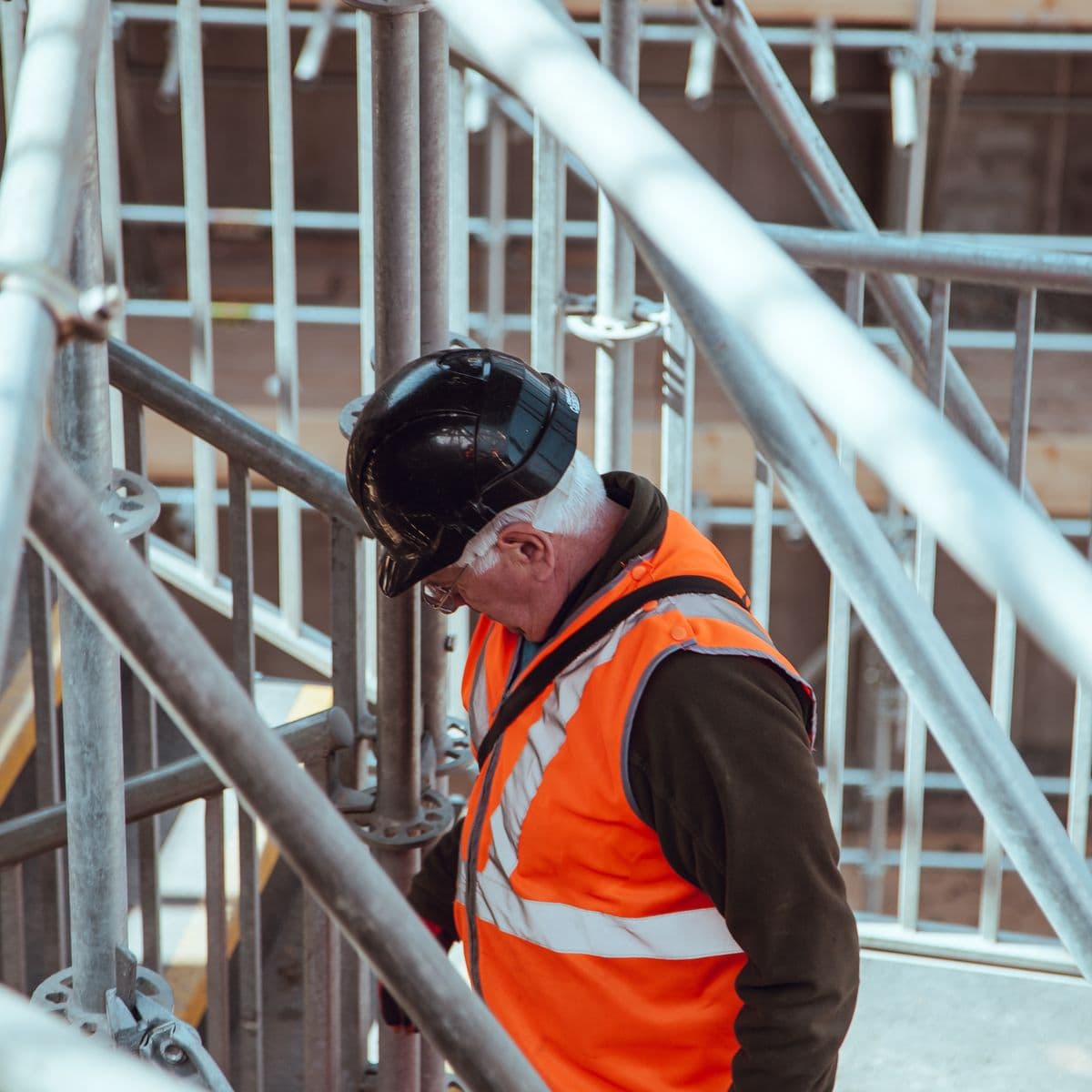 Site worker in a hard hat and high-visibility vest checking scaffolding on a building site