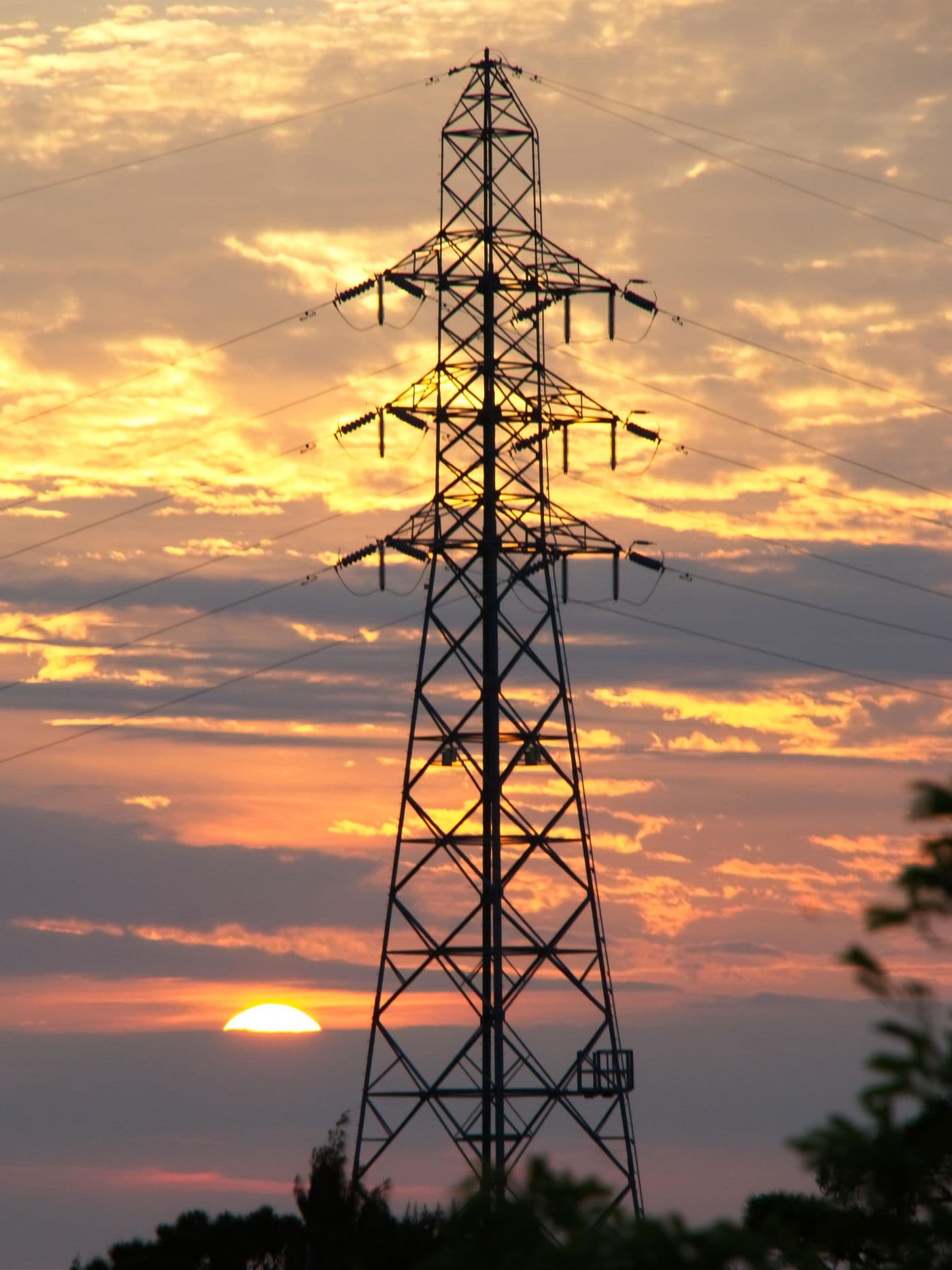 High-voltage transmission tower silhouetted against a golden sunset sky