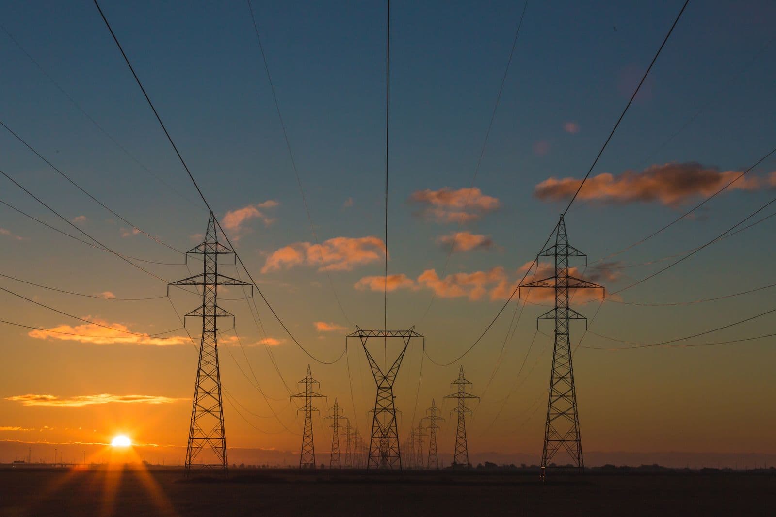 Lines of high-voltage pylons stretching to the horizon at sunset