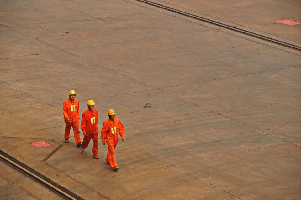 Three workers in orange coveralls and hard hats walking across a steel deck